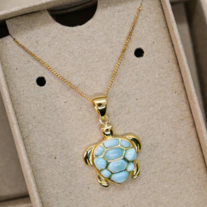 Turtle-shaped pendant necklace in a cardboard box on a patterned surface