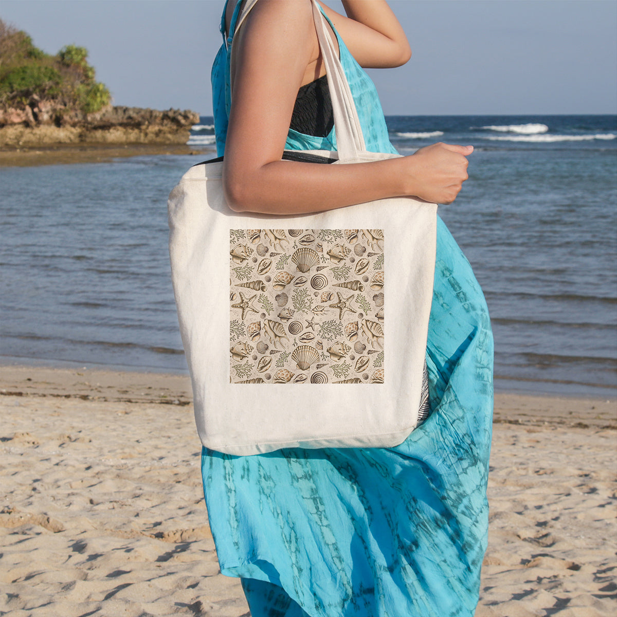 Person holding a tote bag with a shell pattern on a beach
